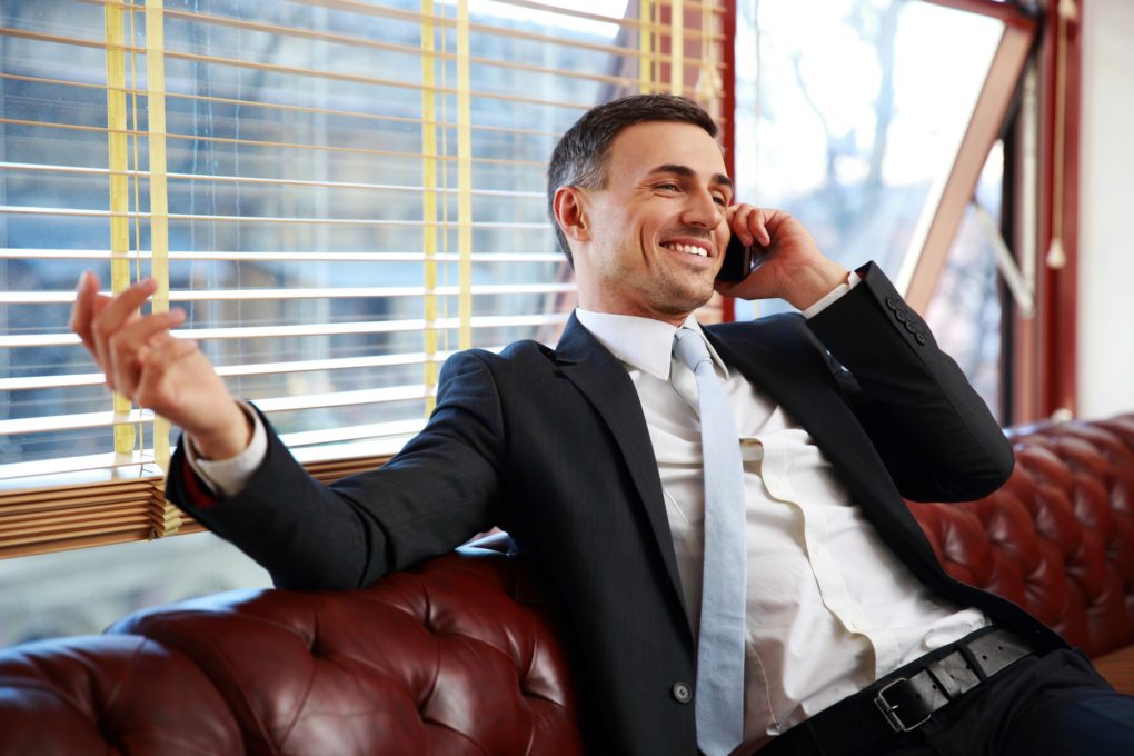 Happy businessman sitting and talking on the phone at office