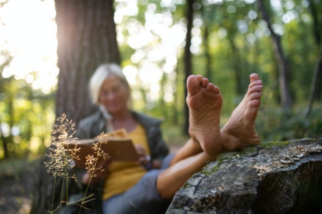 Senior woman relaxing and reading book outdoors in forest