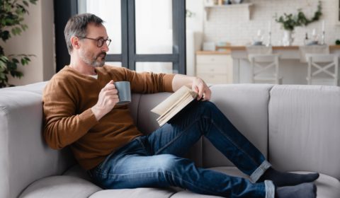 Relaxed Caucasian mature man father husband reading book, preparing for lessons tutoring