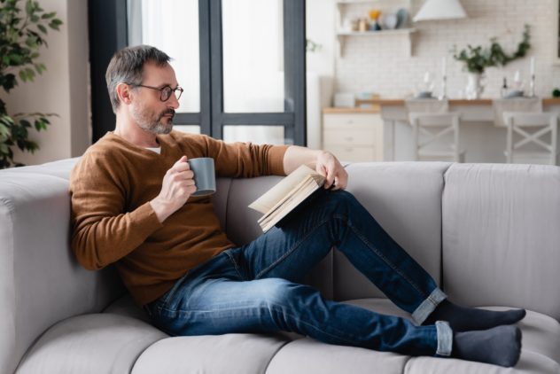 Relaxed Caucasian mature man father husband reading book, preparing for lessons tutoring